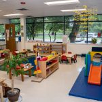 Colorful preschool classroom with toys, tables, and play equipment.