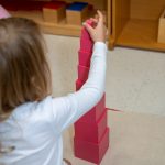 Child stacking pink blocks in Montessori classroom setting.