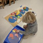 Child assembling world map puzzle on classroom floor.