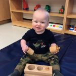 Baby playing with wooden Montessori toy on mat