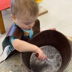 Toddler playing with bubbles in large brown container
